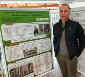 Dr Pernaci Michael devant son poster au congrès de phytopathologie à Aussois en France. Le poster est intitulé "First report of basal stem rot caused by Ganoderma ryvardeni on oil palm in Benin Republic"